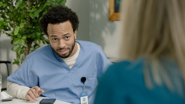 Two healthcare workers sitting across from one another, male looks surprised by something the female co-worker just said